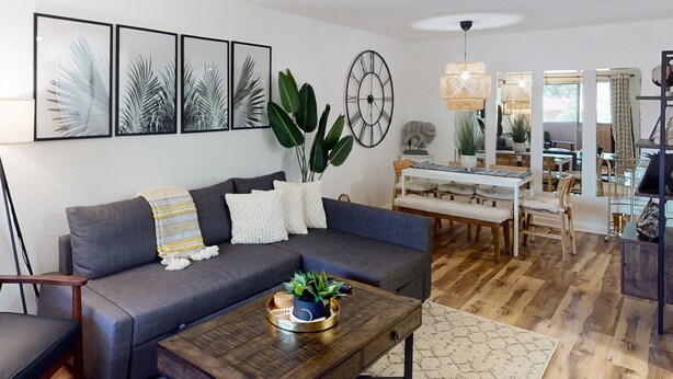 Un salon moderne avec un canapé gris, une table basse en bois et un coin repas comprenant une table et des chaises blanches.