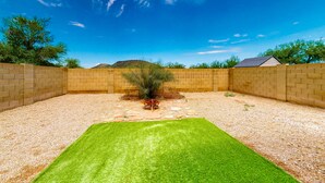 A backyard with a well-maintained lawn, a small tree, and a brick wall. - Retro home with enclosed yard, covered patio, grill, firepit, AC, & washer/dryer (Glendale)