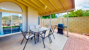 A covered patio area with a glass table and chairs, a barbecue grill, and a trash can. - Retro home with enclosed yard, covered patio, grill, firepit, AC, & washer/dryer (Glendale)