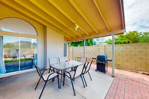 A covered patio area with a glass table and chairs, a barbecue grill, and a trash can. - Retro home with enclosed yard, covered patio, grill, firepit, AC, & washer/dryer (Glendale)