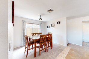 A dining area with a wooden table and chairs, a ceiling light, and a window with curtains. - Retro home with enclosed yard, covered patio, grill, firepit, AC, & washer/dryer (Glendale)