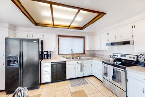 Cocina moderna con armarios blancos, un refrigerador negro, lavavajillas, estufa y ventana con persianas.