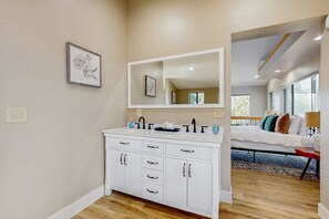 A modern bathroom with a large mirror, white cabinetry, and a wooden floor. - Spacious home w/ large yard, deck, mountain view, fire pit & grill (Flagstaff)