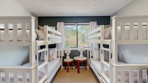 Een kamer met stapelbedden, een klein tafeltje en een raam met gordijnen.