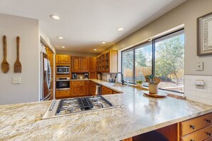 A modern kitchen with wooden cabinets, a stainless steel stove, and a large window offering a view of the outdoors. - Spacious home w/ large yard, deck, mountain view, fire pit & grill (Flagstaff)