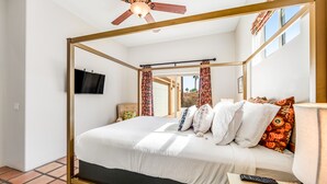 A four-poster bed with a television mounted on the wall, a ceiling fan, and a view of the outdoors through an open door. - Mountain-view home with private pool & spa, near trails - 3BR #220080 (La Quinta)