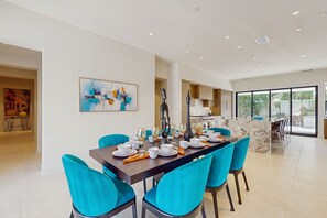 A modern dining area with a long table set for six, surrounded by turquoise chairs.