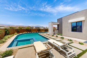A modern outdoor pool area with lounge chairs and a view of mountains in the background.