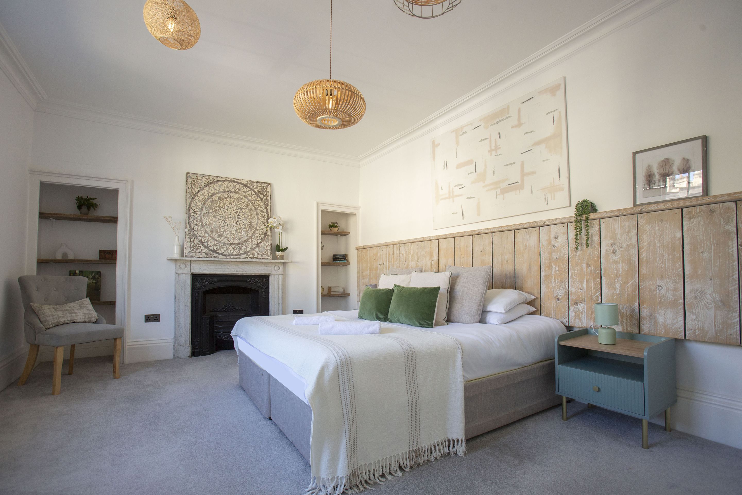 A bedroom with a bed, bedside table, chair, fireplace, and artwork.