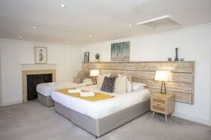 Un lit double avec une tête de lit en bois, deux tables de chevet avec des lampes, une cheminée et des œuvres d’art accrochées aux murs.