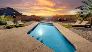 A rectangular swimming pool with a clear blue water surface, surrounded by beige stone tiles. There are two lounge chairs on each side of the pool, and a palm tree is visible to the right. - Charming & sunlit villa with private pool, patio, & firepit - near golf & trails (Mesa)