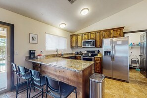 Une cuisine dotée de plans de travail en granit, de meubles en bois, d’appareils électroménagers en acier inoxydable et d’une poubelle.