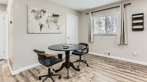 Ein modernes Zimmer mit rundem Tisch, zwei Stühlen, einer Weltkarte als Bild, einem Fenster mit Vorhängen und einer Heizung.