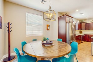 A dining area with a round wooden table, blue chairs, a hanging light fixture, and a window with blinds. - Modern home w/ two master suites & private balcony, desk space, & central A/C (Flagstaff)