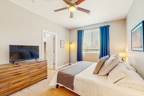 A bedroom with a bed, a TV on a wooden dresser, a ceiling fan, and a window with curtains. - Modern home w/ two master suites & private balcony, desk space, & central A/C (Flagstaff)