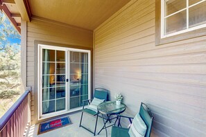 A covered porch with a sliding glass door leading to a bedroom, a small round table, two chairs, and a doormat. - Modern home w/ two master suites & private balcony, desk space, & central A/C (Flagstaff)
