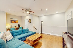 A modern living room with a blue sectional sofa, a wooden coffee table, a ceiling fan, recessed lighting, a floor lamp, and a flat-screen TV. - Modern home w/ two master suites & private balcony, desk space, & central A/C (Flagstaff)