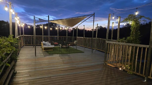 A wooden deck with a canopy, outdoor seating, and string lights. - Cozy-Chic Container Tiny Home + Treehouse Deck (Wagoner)