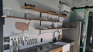 A modern kitchen with wooden cabinets, a stainless steel refrigerator, and a black countertop. - Cozy-Chic Container Tiny Home + Treehouse Deck (Wagoner)