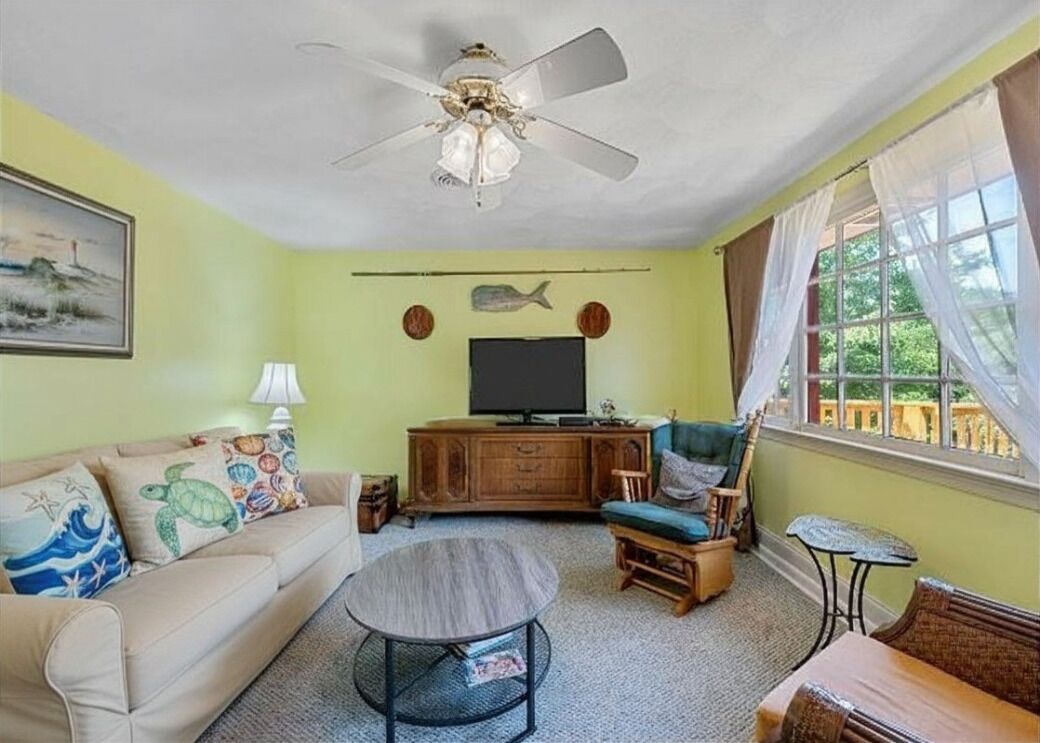 Ein Wohnzimmer mit Sofa, Sessel, Couchtisch, Fernseher und Deckenventilator.