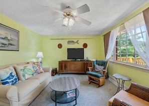 Ein Wohnzimmer mit Sofa, Sessel, Couchtisch, Fernseher und Deckenventilator.