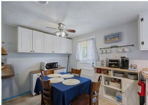A compact kitchen with white cabinets, a dining table with plates, a ceiling fan, and a window with curtains. - 3-bedroom house in lovely Sandbridge Beach-Budget Getaway (Virginia Beach)
