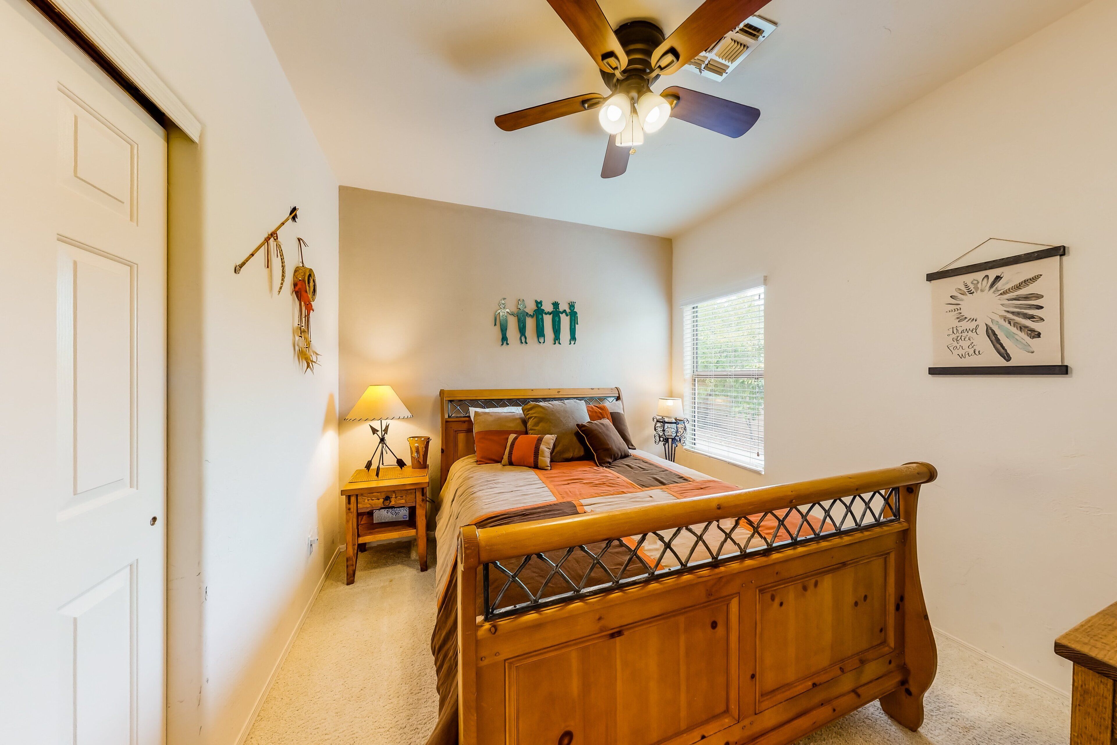 Quarto com cama de madeira, ventilador de teto, mesa de cabeceira, luminária na parede e janela com persianas.