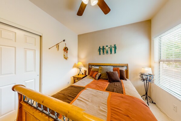 A bedroom with a bed, bedside tables, a ceiling fan, a wall decoration, and a window with blinds.