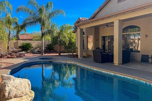 A backyard with a swimming pool, patio furniture, and palm trees.