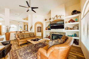 A spacious living room with leather sofas, a flat-screen TV, and decorative items on shelves.