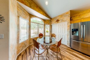 A kitchen with a glass dining table, wooden chairs, a stainless steel refrigerator, and a white door.