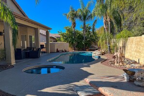 A backyard with a swimming pool, outdoor furniture, and palm trees.