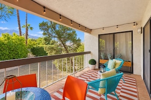 A balcony with a checkered floor, two chairs, a table, and a potted plant. - Mtn-view 2nd-floor renovated condo near trails with 4 pools, pool spas, balcony (Palm Springs)