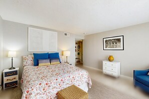 A bedroom with a bed, bedside tables, a lamp, a chair, a shelf with items, and a framed picture on the wall. - Mtn-view 2nd-floor renovated condo near trails with 4 pools, pool spas, balcony (Palm Springs)