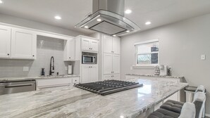 A modern kitchen with white cabinetry, a large marble island, and a built-in microwave. - Group Getaway Near Eufaula Lake & Boat Ramp! (Eufaula)
