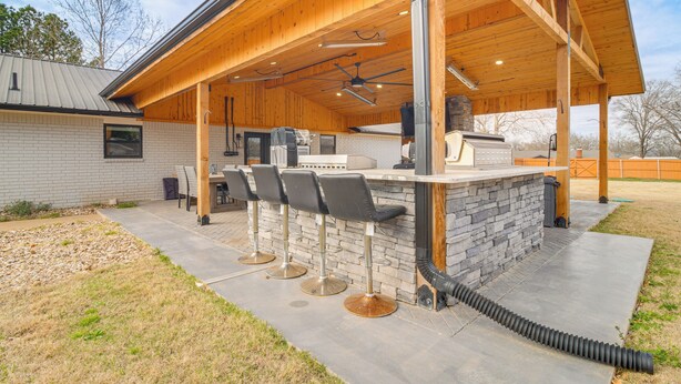 A covered outdoor bar area with stone countertops, bar stools, and a ceiling fan. - Group Getaway Near Eufaula Lake & Boat Ramp! (Eufaula)