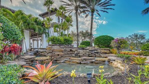 A garden with a pond, stone wall, and various plants. - Luxury Waterfront Living! Naples Resort Condo (Naples)
