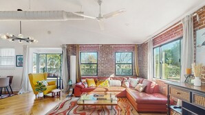 A spacious living room with a red leather sofa, a glass coffee table, and a brick wall. - Sunny downtown home with private pool, hammock, enclosed backyard, grill, patio (Phoenix)
