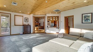 Ett rymligt vardagsrum med ett högt träpanelat tak, en beige soffa och ett kök med träskåp.