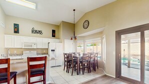 Una cocina amplia con armarios blancos, un comedor con sillas de madera y un ventanal con vistas al exterior.