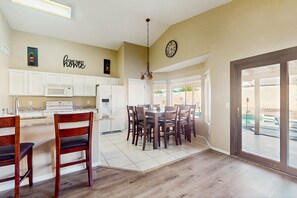 A spacious kitchen with white cabinets, a dining area with wooden chairs, and a large window offering a view of the outdoors. - Modern home w/ private heated pool, backyard w/ patio & BBQ grill (Mesa)