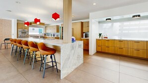 A modern kitchen with a marble island, wooden cabinets, and red pendant lights. - Poolside Paradise in the Desert – Your Perfect Palm Springs Escape Awaits. (Palm Springs)