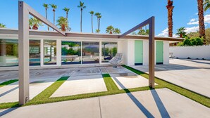 A modern house with a glass facade, a patio with artificial grass, and palm trees in the background. - Poolside Paradise in the Desert – Your Perfect Palm Springs Escape Awaits. (Palm Springs)