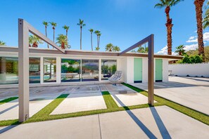 Ein modernes Haus mit Glasfassade, einer Terrasse mit künstlichem Rasen und Palmen im Hintergrund.
