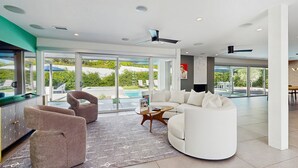 A modern living room with a large window, a pool, and a ceiling fan. - Poolside Paradise in the Desert – Your Perfect Palm Springs Escape Awaits. (Palm Springs)