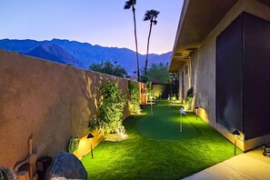 Un espacio exterior cuidado con césped verde, un pequeño campo de práctica de golf y un muro de hormigón.