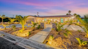 A hotel with a paved driveway, stone pillars, and palm trees. - Designer dream with fireplace, game room, private pool, outdoor kitchen, firepit (Palm Springs)