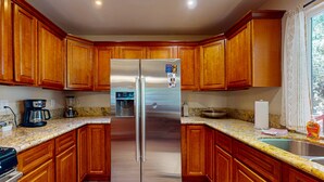 Eine Küche mit Holzausstattung, einem Edelstahlkühlschrank, Granit Arbeitsplatten und einem Fenster mit Vorhängen.