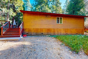 Een houten chalet met een rood dak, een klein raam en een trap naar een overdekt terras.