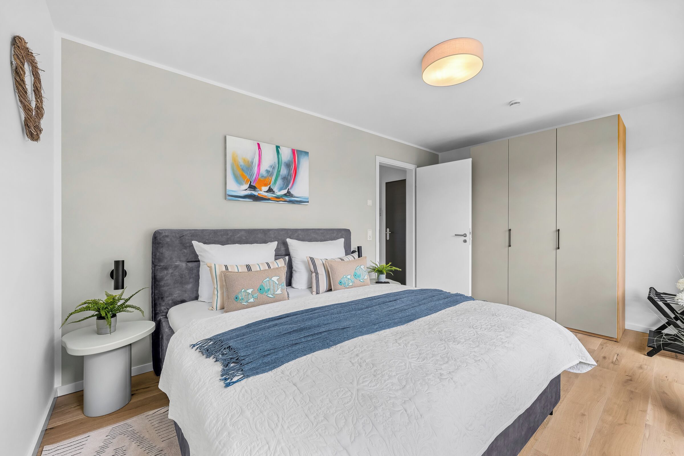 Une chambre à coucher moderne avec un grand lit, un tableau, une table de chevet avec une plante et une armoire.